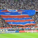 Torcedores exibem uma grande faixa com a camisa do Fortaleza nas arquibancadas de um estádio lotado.