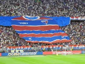 Torcedores exibem uma grande faixa com a camisa do Fortaleza nas arquibancadas de um estádio lotado.