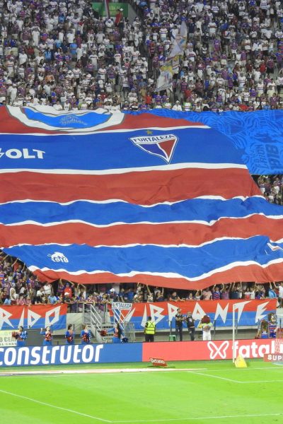 Torcedores exibem uma grande faixa com a camisa do Fortaleza nas arquibancadas de um estádio lotado.