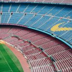 Vista aérea do Camp Nou vazio, com o campo de futebol e as arquibancadas coloridas do estádio do Barcelona.