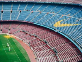 Vista aérea do Camp Nou vazio, com o campo de futebol e as arquibancadas coloridas do estádio do Barcelona.
