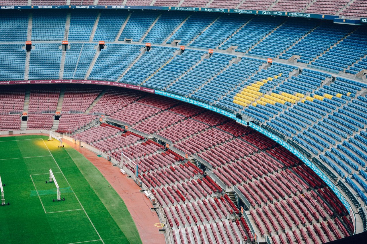 Vista aérea do Camp Nou vazio, com o campo de futebol e as arquibancadas coloridas do estádio do Barcelona.