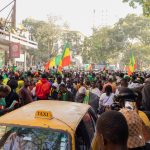 Multidão celebra em uma rua de Dakar enquanto acena com bandeiras do Senegal.