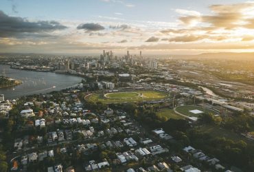 Vista aérea de Brisbane ao entardecer, com o rio sinuoso, a paisagem urbana e o horizonte da cidade.