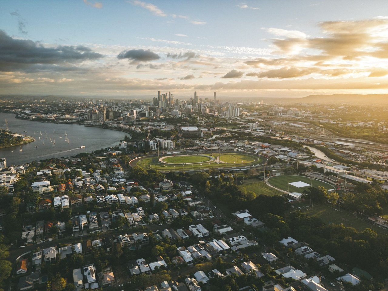 Vista aérea de Brisbane ao entardecer, com o rio sinuoso, a paisagem urbana e o horizonte da cidade.