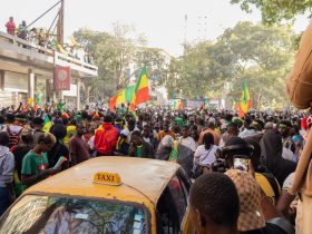 Multidão celebra em uma rua de Dakar enquanto acena com bandeiras do Senegal.