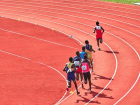 Atletas disputam uma corrida em uma pista curva ao ar livre.