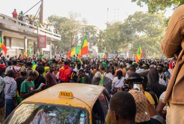 Multidão celebra em uma rua de Dakar enquanto acena com bandeiras do Senegal.