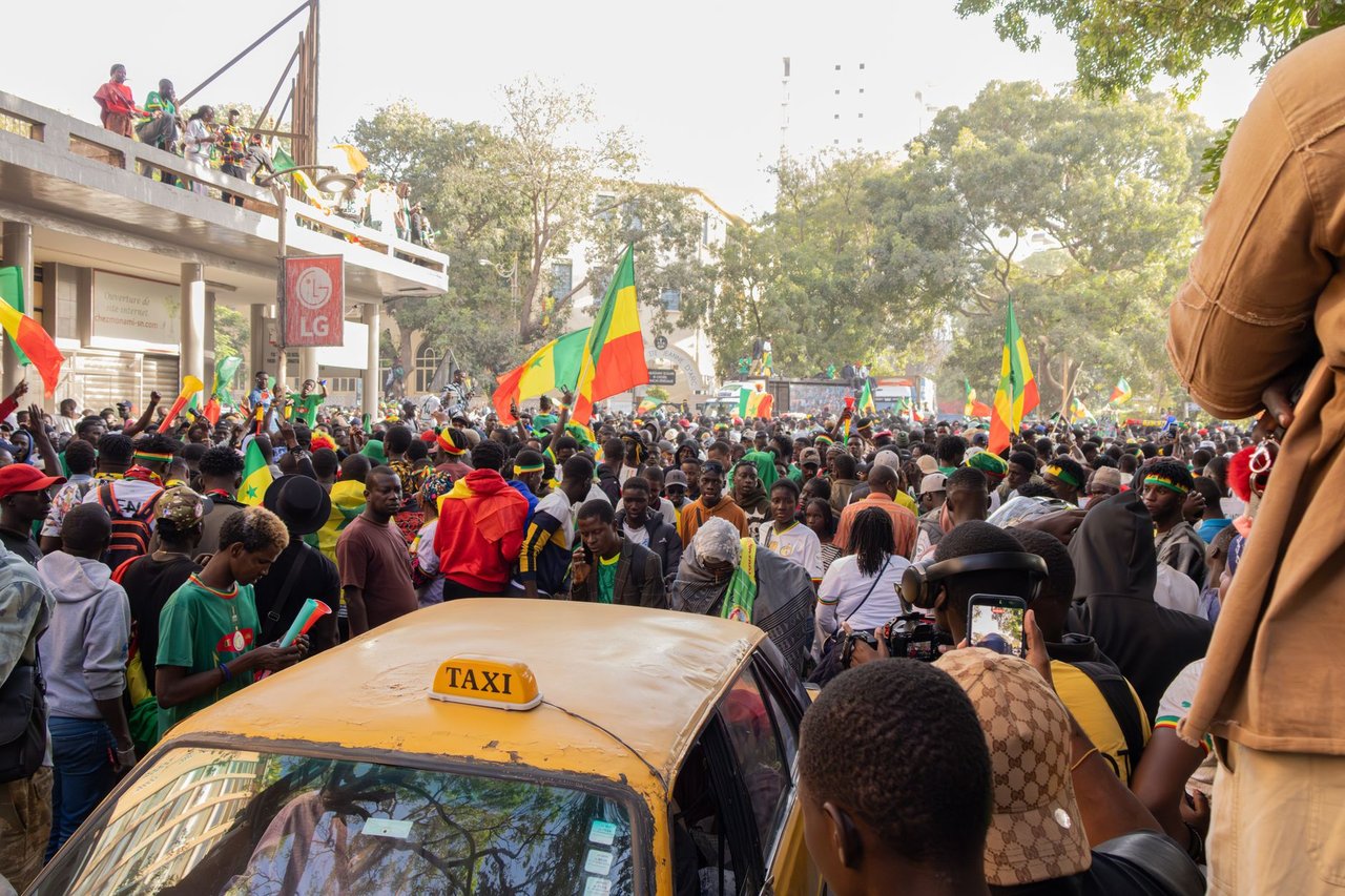 Multidão celebra em uma rua de Dakar enquanto acena com bandeiras do Senegal.
