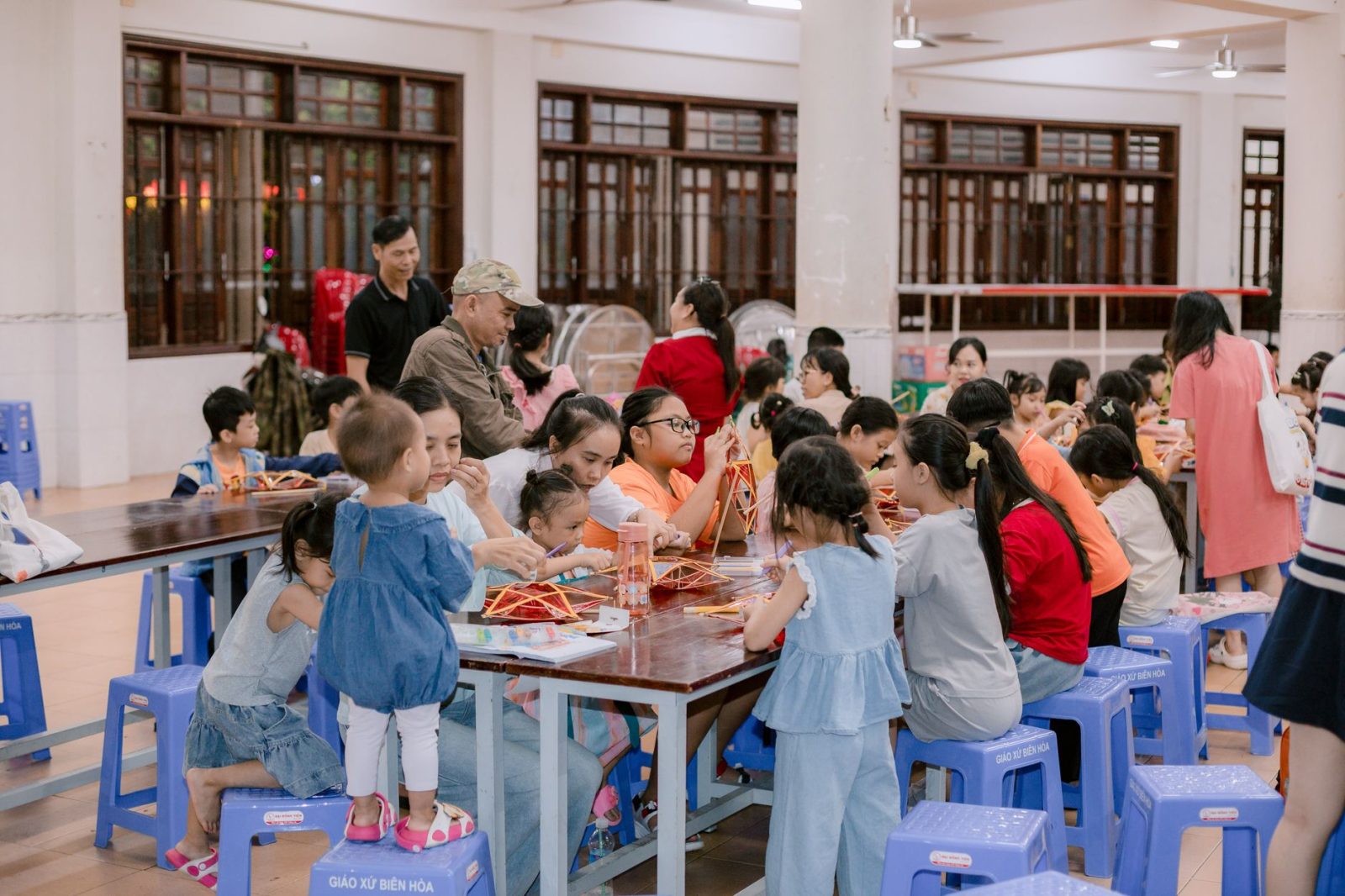 Crianças e adultos participam de uma atividade artesanal em um espaço comunitário.
