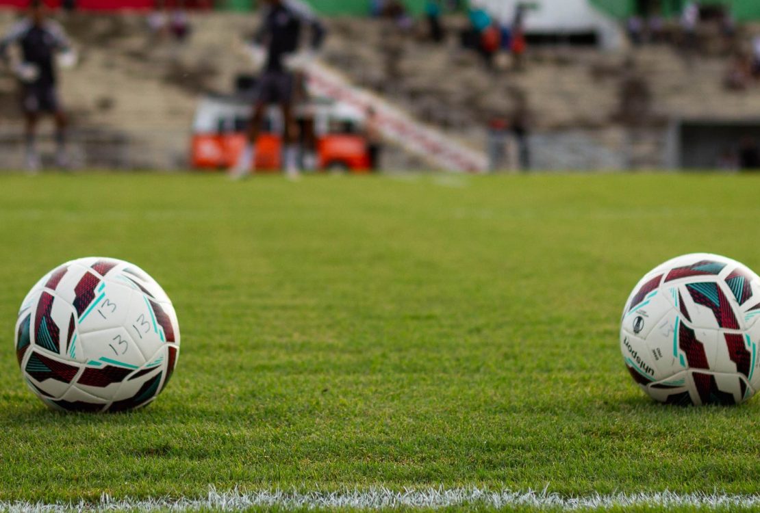 Duas bolas de futebol sobre o gramado de um estádio antes de uma partida.