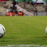 Duas bolas de futebol sobre o gramado de um estádio antes de uma partida.