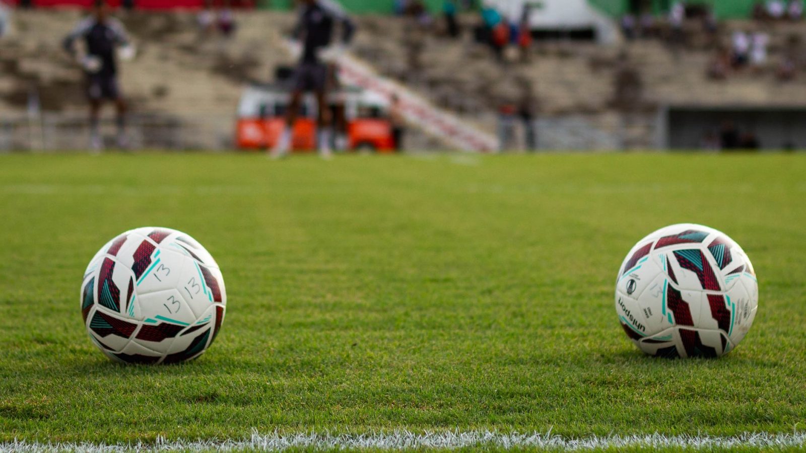 Duas bolas de futebol sobre o gramado de um estádio antes de uma partida.